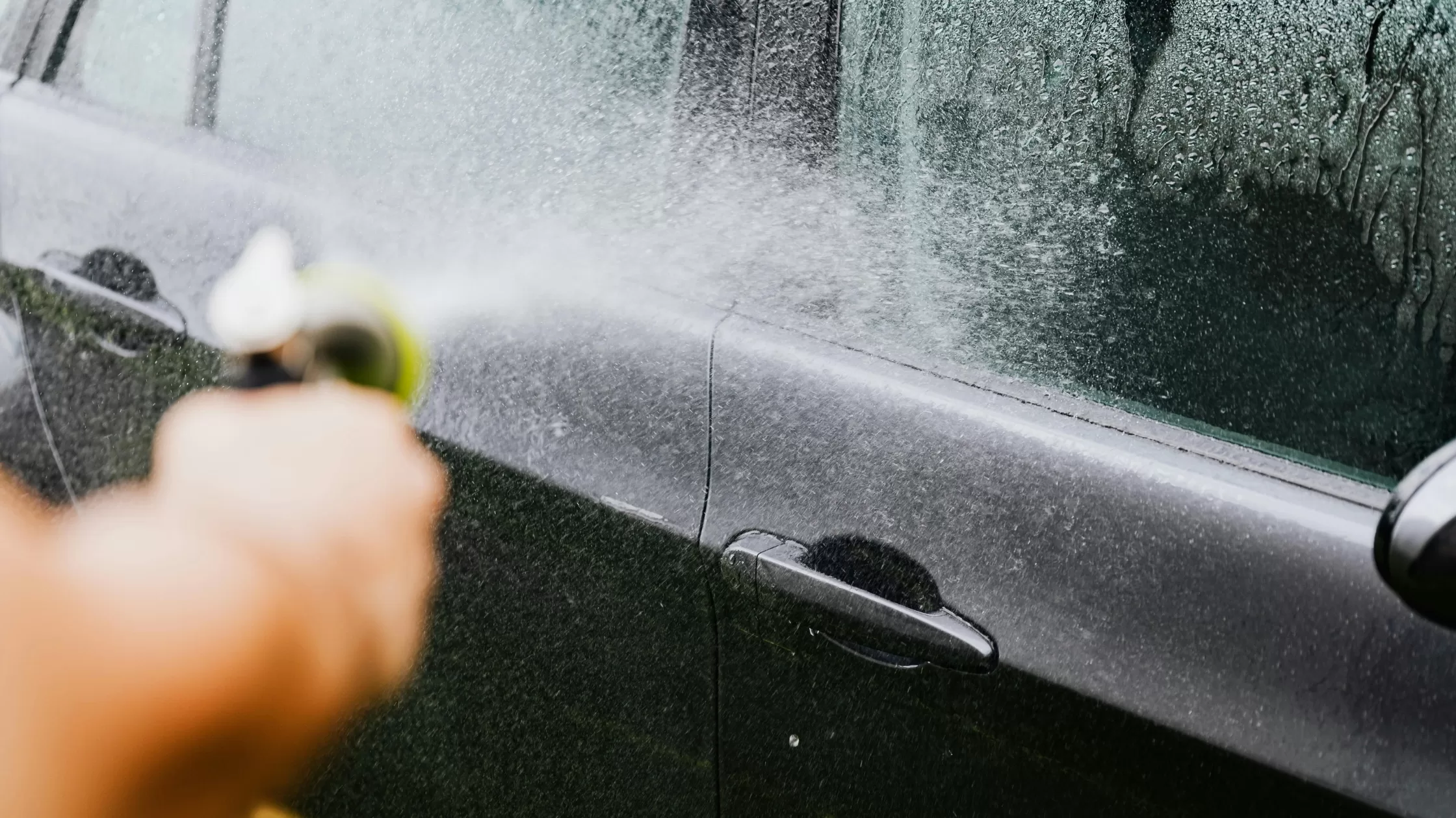 person washing black car with a water hose